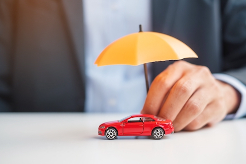 Business man holding umbrella over red toy car